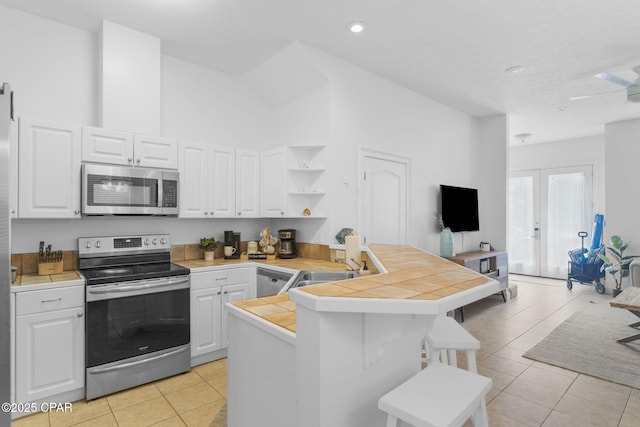 kitchen featuring white cabinetry, light tile patterned floors, tile counters, kitchen peninsula, and stainless steel appliances