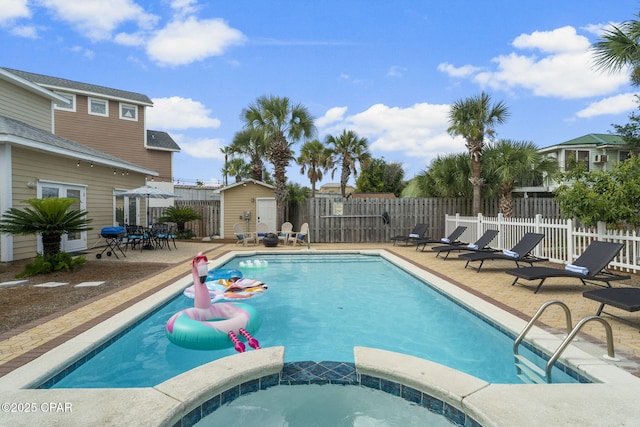 view of pool featuring an in ground hot tub, a patio, and a storage shed