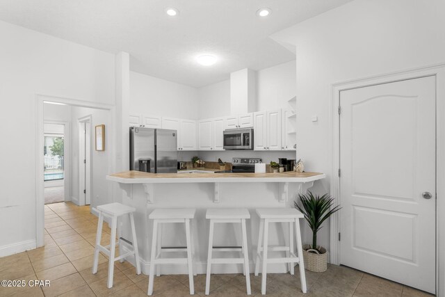 kitchen with white cabinetry, stainless steel appliances, kitchen peninsula, and a kitchen bar