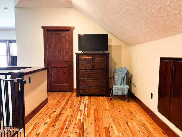 sitting room with lofted ceiling, a textured ceiling, light wood-type flooring, and baseboards