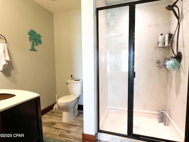 full bathroom with a stall shower, baseboards, toilet, wood finished floors, and vanity