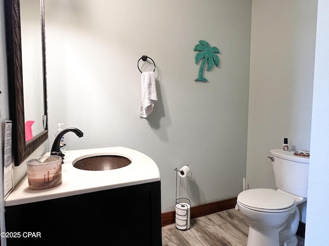 half bath featuring toilet, wood finished floors, vanity, and baseboards