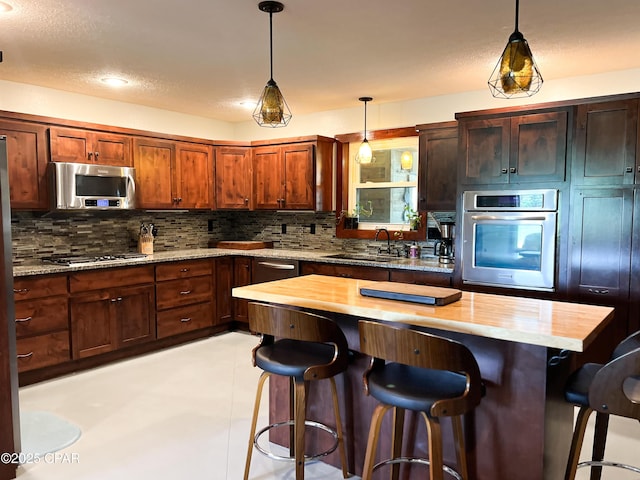 kitchen with a breakfast bar, decorative light fixtures, appliances with stainless steel finishes, backsplash, and a sink