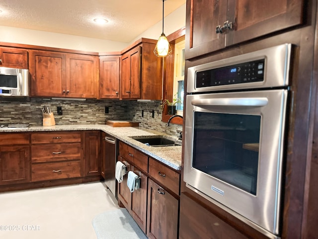 kitchen featuring pendant lighting, tasteful backsplash, a sink, stainless steel appliances, and light stone countertops