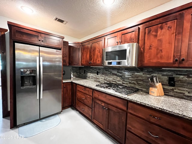 kitchen with appliances with stainless steel finishes, a textured ceiling, tasteful backsplash, and light stone countertops