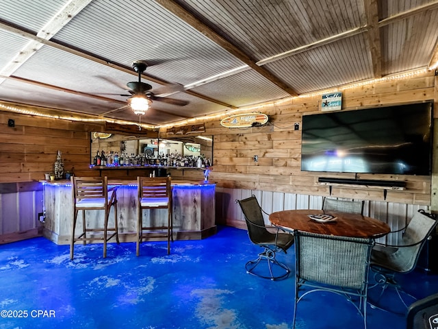 bar featuring a ceiling fan, concrete flooring, wooden walls, and a dry bar