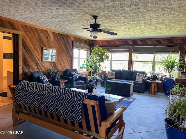 living area featuring wooden walls, tile patterned flooring, and ceiling fan