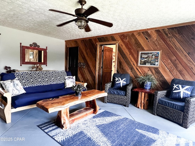 living area with wood walls, a ceiling fan, a textured ceiling, and tile patterned flooring