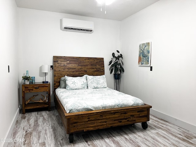 bedroom featuring light wood-style flooring, a wall mounted AC, and baseboards