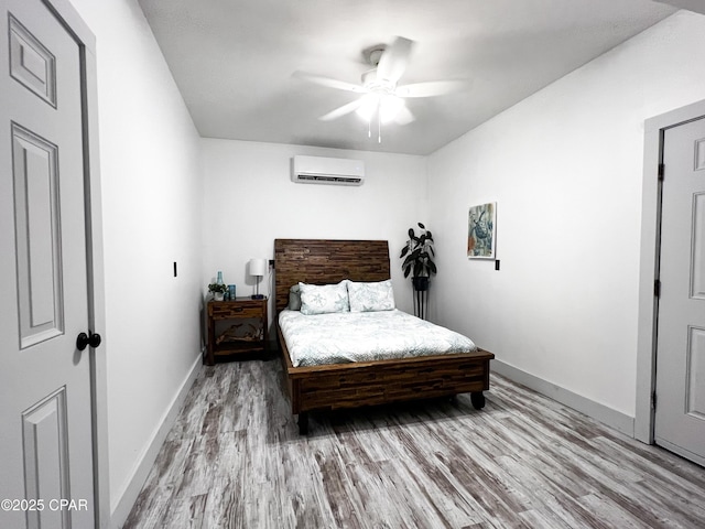 bedroom featuring ceiling fan, a wall mounted air conditioner, light wood-style flooring, and baseboards