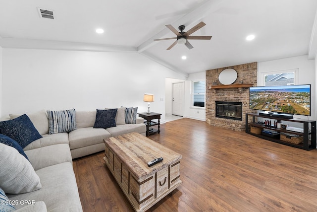 living room featuring dark wood-type flooring, vaulted ceiling with beams, ceiling fan, and a brick fireplace