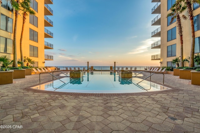 pool at dusk with a water view and a patio