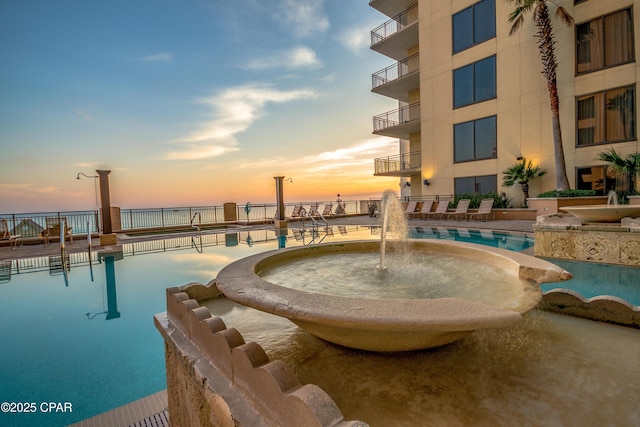 pool at dusk featuring pool water feature and a water view