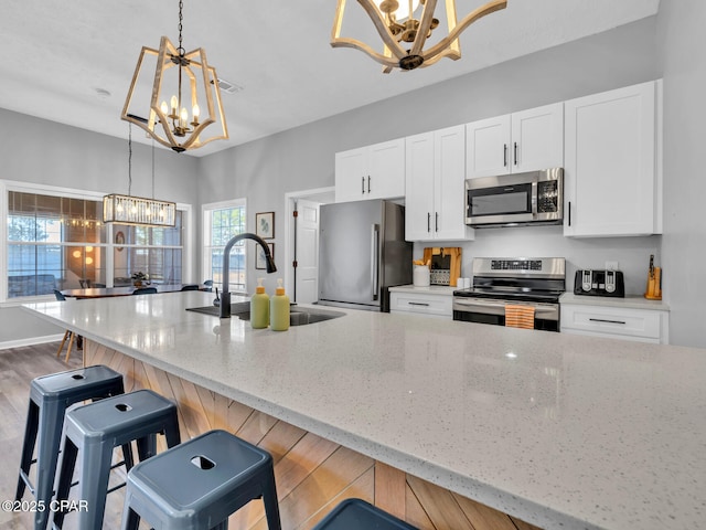 kitchen featuring appliances with stainless steel finishes, light stone counters, decorative light fixtures, a chandelier, and a sink