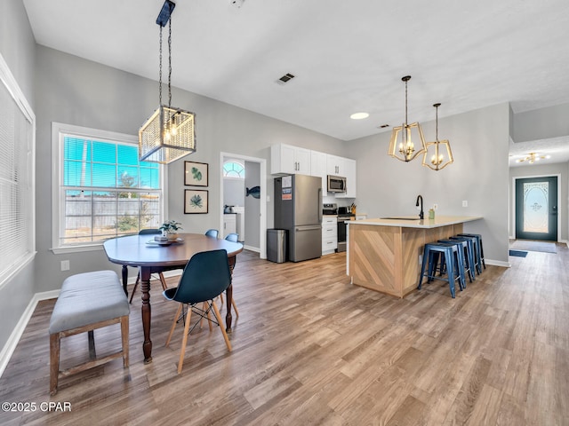 dining area featuring visible vents, light wood-type flooring, an inviting chandelier, and baseboards