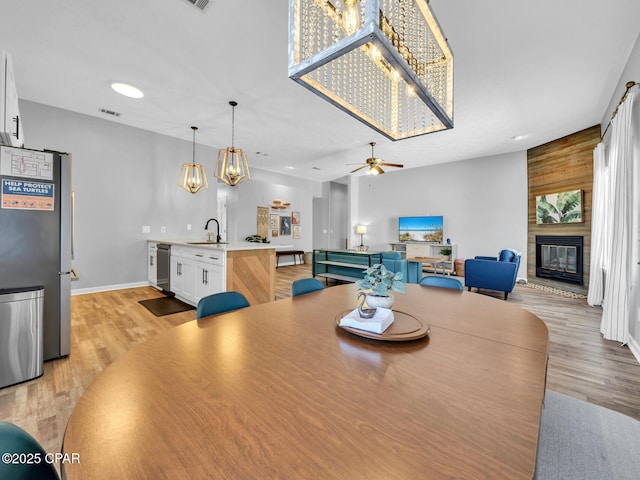 dining room with a large fireplace, visible vents, ceiling fan, and light wood finished floors