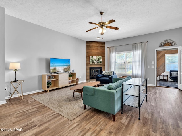 living room with ceiling fan, a textured ceiling, hardwood / wood-style floors, and a fireplace