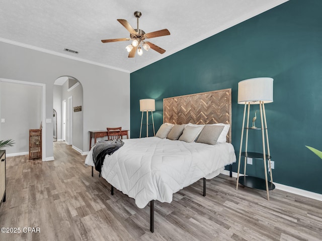 bedroom featuring an accent wall, arched walkways, baseboards, and wood finished floors