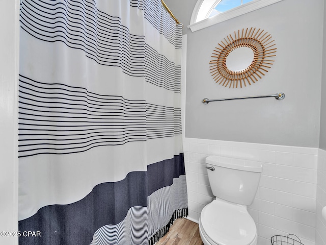 full bathroom featuring a wainscoted wall, tile walls, toilet, and wood finished floors