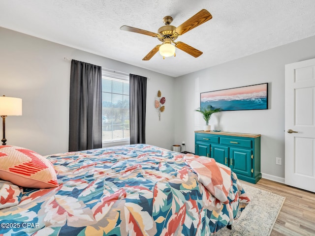 bedroom featuring light wood-style floors, ceiling fan, baseboards, and a textured ceiling