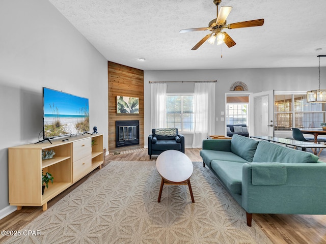 living area with light wood finished floors, wooden walls, a textured ceiling, a fireplace, and ceiling fan with notable chandelier