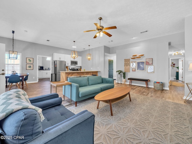 living room featuring visible vents, light wood-style flooring, baseboards, and ceiling fan with notable chandelier