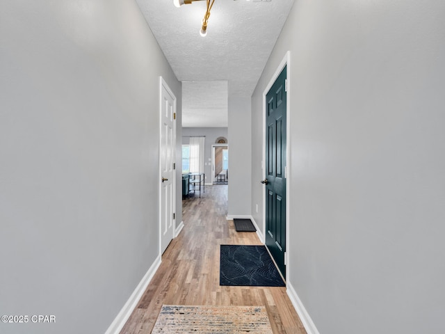 corridor featuring light wood finished floors, baseboards, and a textured ceiling