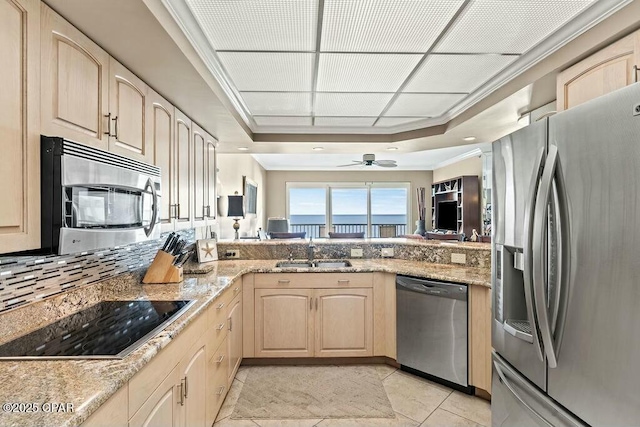 kitchen with light stone countertops, a tray ceiling, stainless steel appliances, light brown cabinetry, and a sink