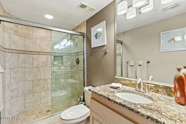 bathroom featuring toilet, vanity, a shower stall, and visible vents