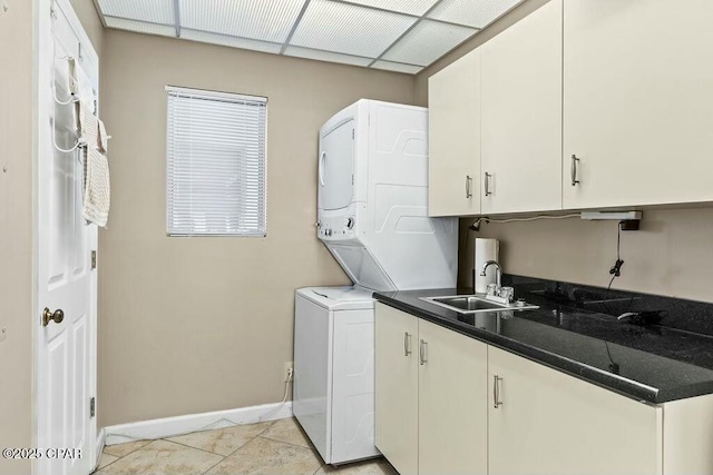 laundry area with cabinet space, light tile patterned floors, baseboards, stacked washer / drying machine, and a sink