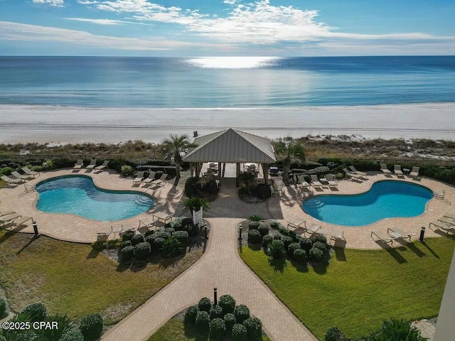 community pool featuring a gazebo, a patio area, a beach view, and a water view