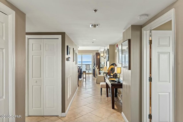 hall featuring light tile patterned flooring, visible vents, and baseboards