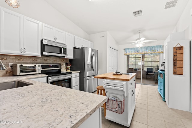 kitchen featuring vaulted ceiling, butcher block countertops, sink, white cabinets, and stainless steel appliances
