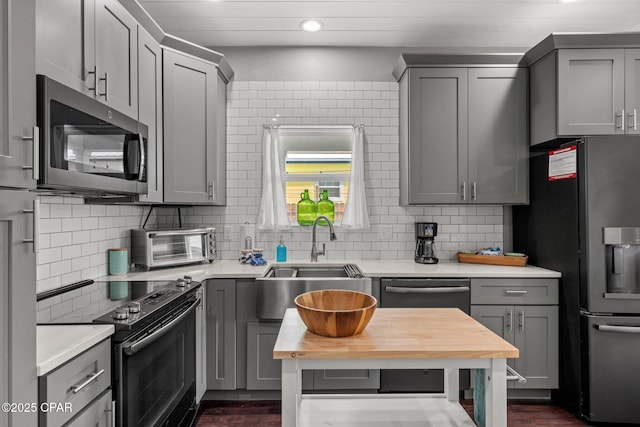 kitchen featuring appliances with stainless steel finishes, gray cabinetry, decorative backsplash, and sink