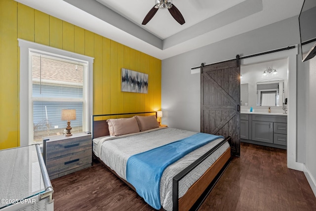 bedroom with ensuite bathroom, a barn door, ceiling fan, dark hardwood / wood-style floors, and a tray ceiling