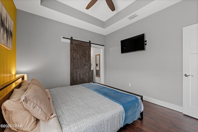 bedroom featuring ceiling fan, dark hardwood / wood-style floors, a raised ceiling, and a barn door