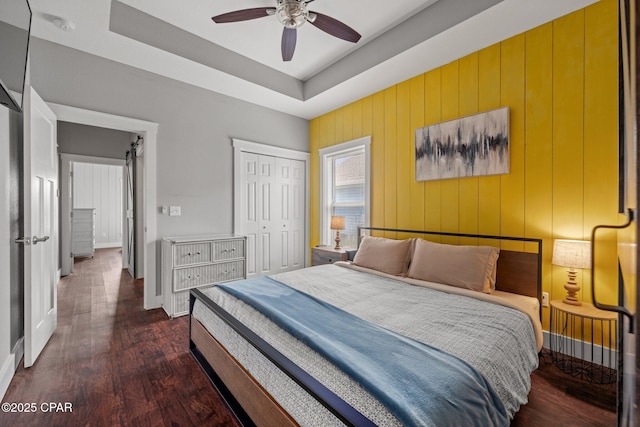 bedroom with ceiling fan, a closet, dark hardwood / wood-style flooring, and a tray ceiling