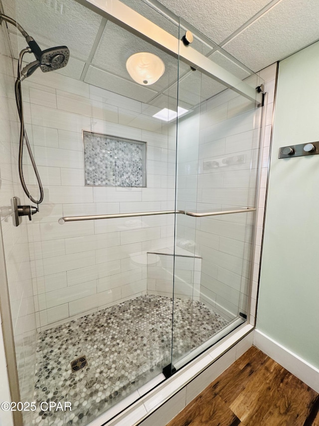 bathroom with wood-type flooring, a paneled ceiling, and a shower with shower door