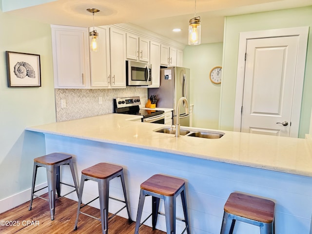 kitchen with sink, hanging light fixtures, appliances with stainless steel finishes, decorative backsplash, and white cabinets