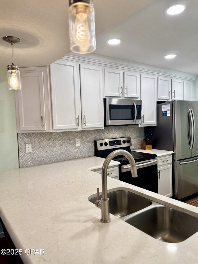 kitchen with sink, appliances with stainless steel finishes, hanging light fixtures, white cabinets, and decorative backsplash