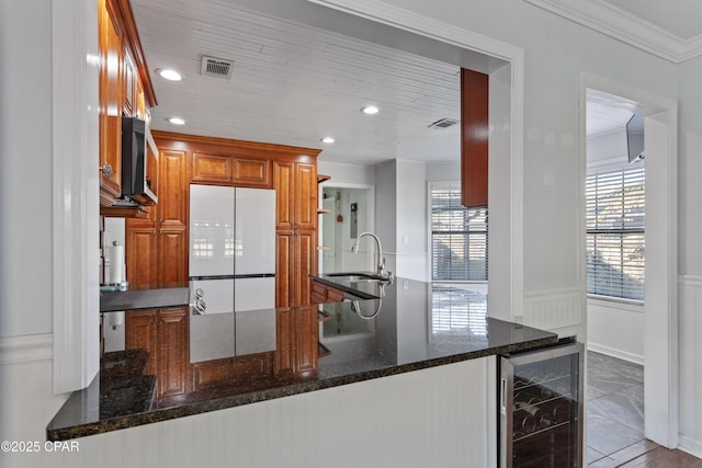 kitchen with wine cooler, dark stone countertops, kitchen peninsula, sink, and crown molding