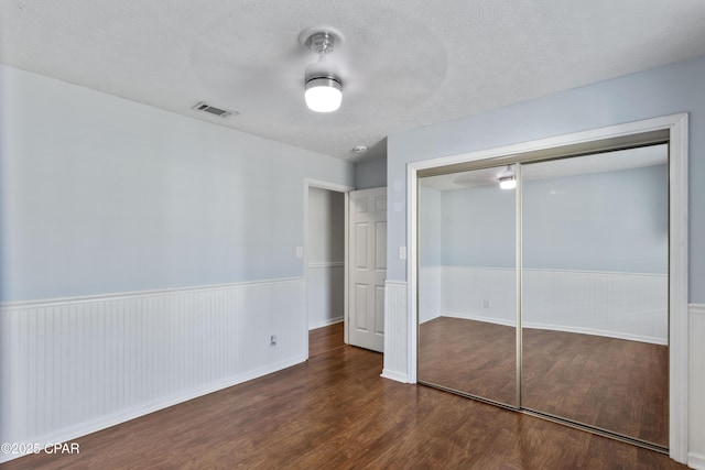 unfurnished bedroom featuring ceiling fan, a textured ceiling, dark hardwood / wood-style floors, and a closet