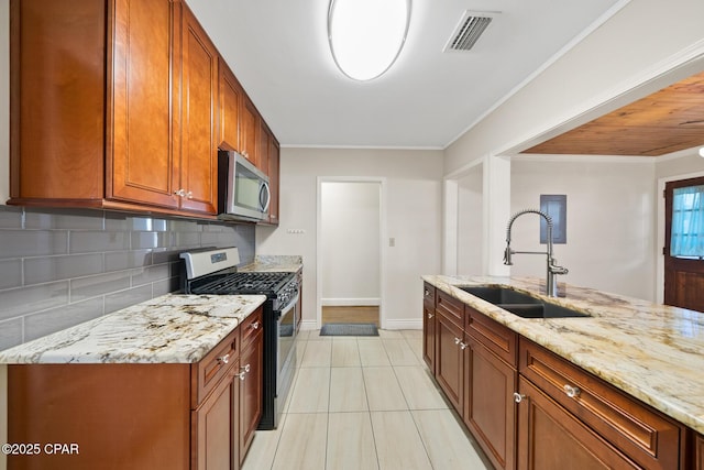 kitchen featuring appliances with stainless steel finishes, sink, backsplash, light stone counters, and a center island with sink