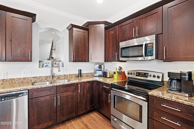 kitchen with sink, light stone counters, light hardwood / wood-style flooring, ornamental molding, and appliances with stainless steel finishes