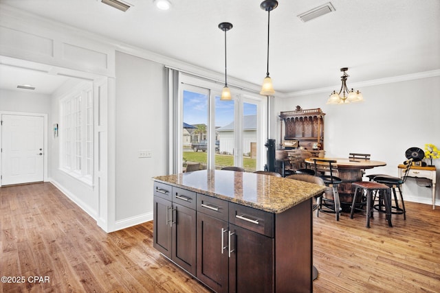 kitchen with dark brown cabinetry, decorative light fixtures, light stone countertops, and light hardwood / wood-style floors