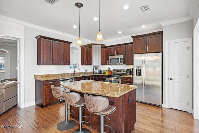 kitchen featuring stainless steel appliances, a kitchen breakfast bar, light stone countertops, a kitchen island, and decorative light fixtures