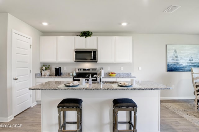 kitchen with stainless steel appliances, light wood-type flooring, visible vents, and a kitchen breakfast bar