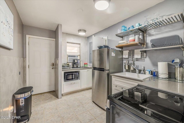 kitchen featuring sink, light tile patterned floors, appliances with stainless steel finishes, tile walls, and white cabinets