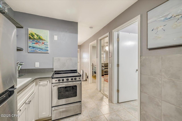 kitchen featuring stainless steel appliances, white cabinetry, tile walls, and light tile patterned floors