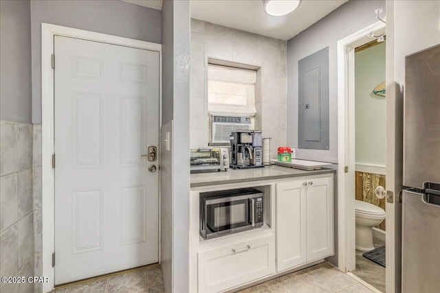 kitchen with white cabinetry, light tile patterned floors, electric panel, and tile walls